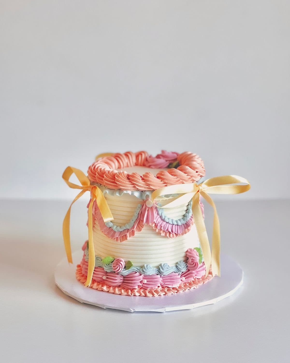 A custom round cake covered in smooth, light pastel yellow frosting. The bottom edge features a thick, intricate, multi-colored piped design resembling vintage floral embroidery. The top edge is finished with a blue scalloped border. Resting on the top of the cake is a handcrafted, sleeping yellow crescent moon, a fluffy white cloud, and delicate white stars. Handcrafted celestial theme cake by PlateStory in Chennai, featuring a smooth pastel base, intricate colorful piped embroidery, and hand-sculpted moon, cloud, and star toppers.