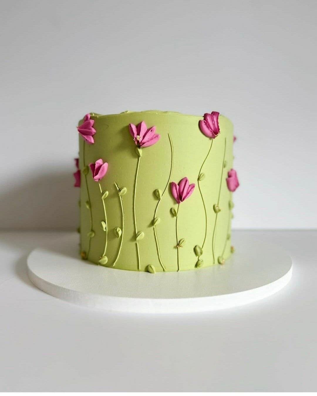 A custom round cake covered in smooth, light green frosting. The design is elegantly accented with detailed, soft pink handcrafted flowers and delicate subtle foliage arrangements. Handcrafted vintage green cake by PlateStory in Chennai, featuring smooth green frosting and elegant pink sugar flowers.